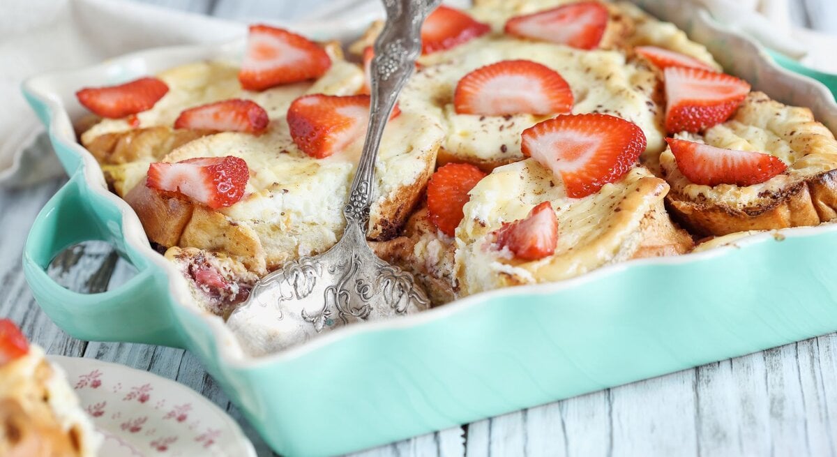 Käsekuchen-Brotauflauf mit Erdbeeren in blauer Auflaufform.  | © Getty Images/StephanieFrey
