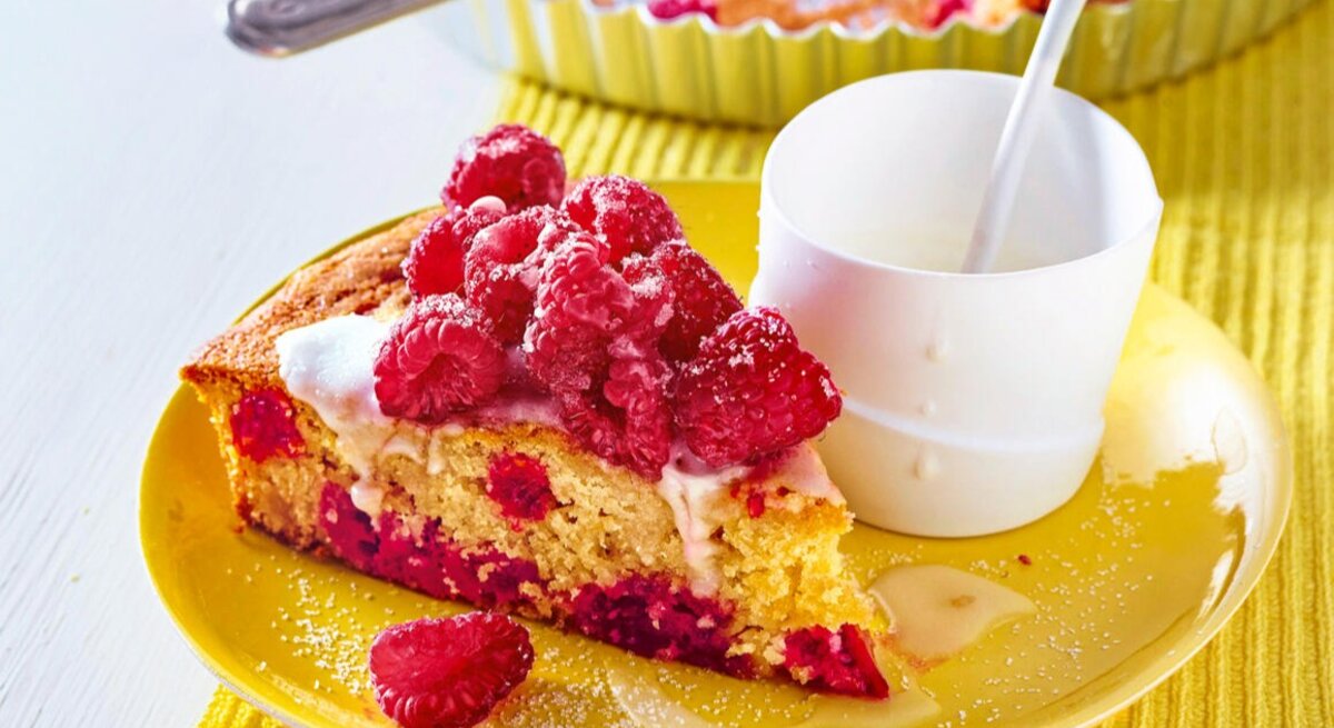Zu sehen ist ein saftiger Himbeer-Buttermilch-Kuchen präsentiert auf einem gelben Teller.