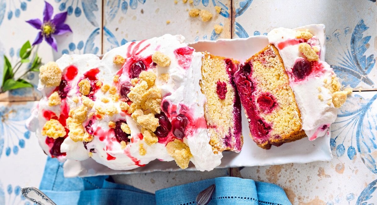 Zu sehen ist ein leckerer Kirschkuchen mit einer cremigen Sahneschicht und knusprigen Streuseln, serviert vor einem blauen Hintergrund