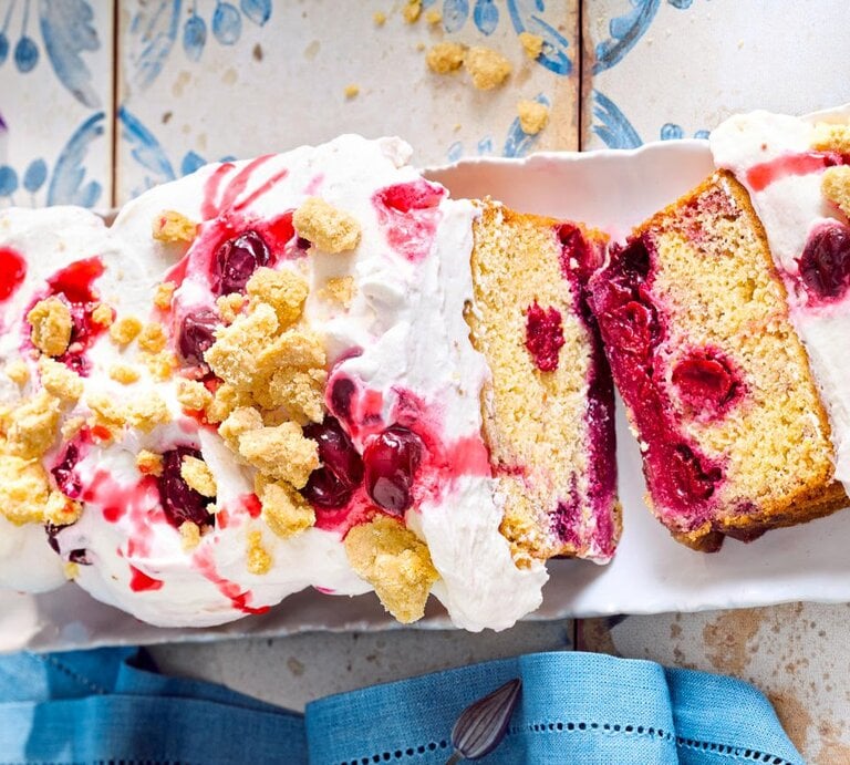 Zu sehen ist ein leckerer Kirschkuchen mit einer cremigen Sahneschicht und knusprigen Streuseln, serviert vor einem blauen Hintergrund | © Eat Club