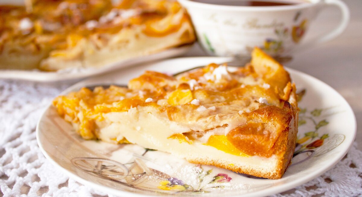 Ein Stück vom Pfirsichkuchen auf einem altmodischen Teller und hellem Holztisch. Alles von der Seite fotografiert.