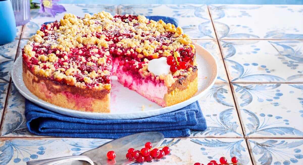 Zu sehen ist ein leckerer Streuselkuchen mit einer Johannesbeercreme, präsentiert vor einem blauen Hintergrund.