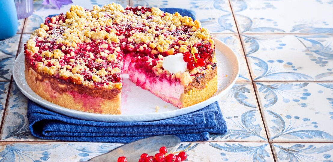 Zu sehen ist ein leckerer Streuselkuchen mit einer Johannesbeercreme, präsentiert vor einem blauen Hintergrund. | © Eat Club