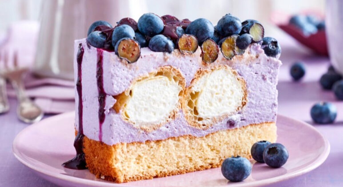 Zu sehen ist eine leckere Windbeuteltorte mit Heidelbeeren vor einem lila Hintergrund