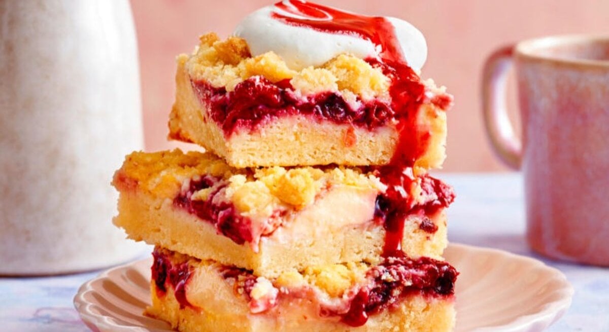 Zu sehen sind Streuselkuchenstücken mit Kirschen und Vanillepudding Füllung, präsentiert vor einem rosa Hintergrund