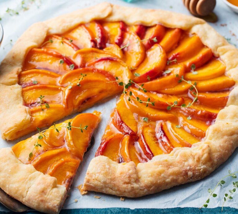 Pfirsich-Galette mit Thymian / Küchenmesser / Schale mit Honig /Nahaufname / Draufsicht | © Getty Images / AnnaPustynnikova