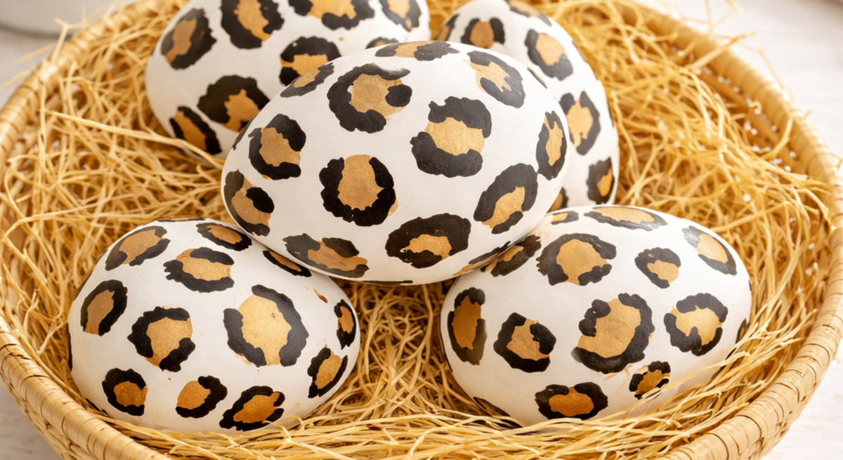 Dekorierte Ostereier im Leopardenlook ruhen in einem runden Korb aus Naturmaterial, umgeben von feinem Stroh auf heller Holzfläche.