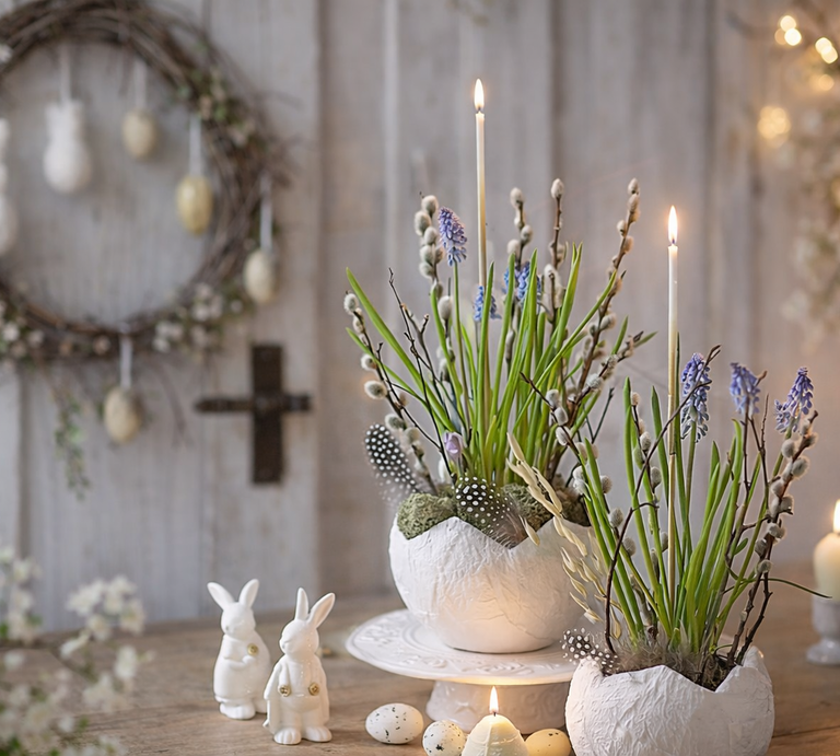 Frühlingshafte Osterdeko mit bepflanzter Eierschale aus Toilettenpapier, Kerzen, Weidenkätzchen und weißen Hasenfiguren auf Holztisch vor Kranz und Kreuz. | © Generiert mit KI (Erstellt mit ChatGPT) 