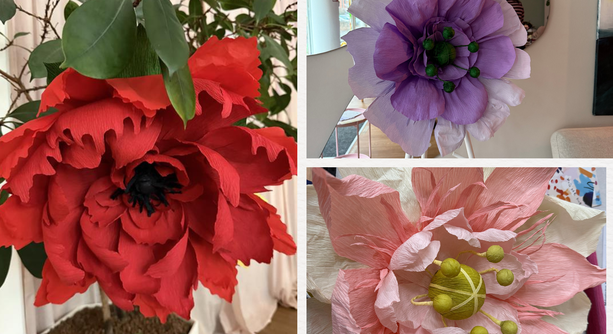 Große rote, lila und zartrosa XXL-Papierblumen mit detailreichen Blütenblättern stehen und liegen dekorativ in hellem Innenraum.
