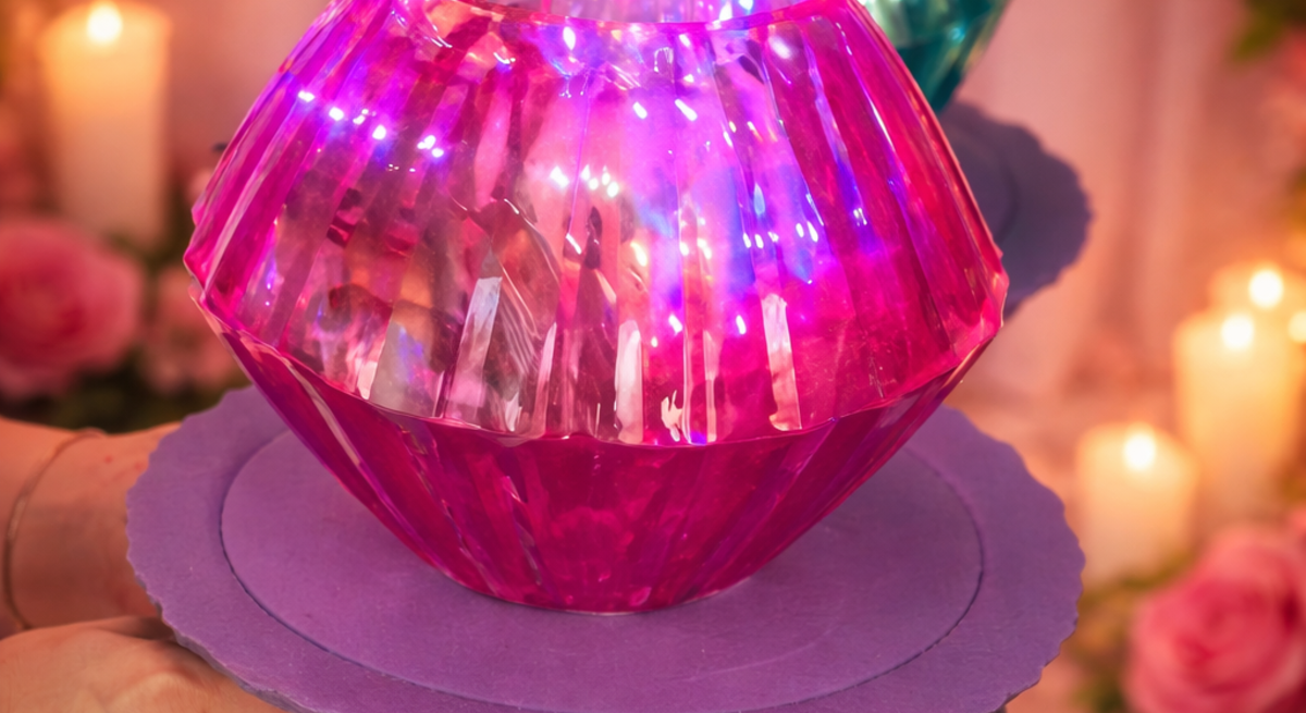 Ein selbst gebastelter Diamantring aus pinkem und türkisfarbenem Glas leuchtet auf einer lilafarbenen Halterung vor Kerzen und Rosen.