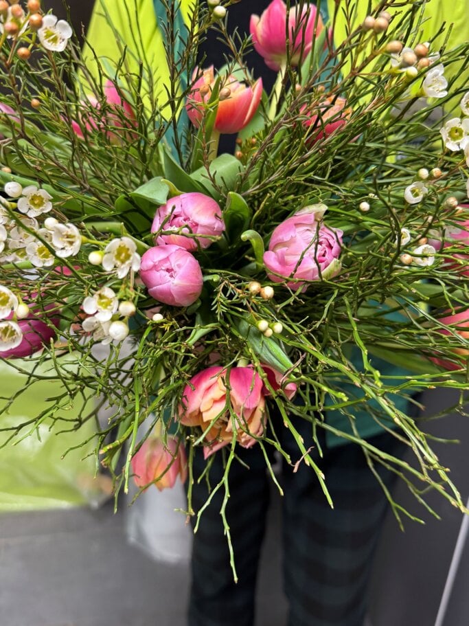 Frischer Strauß aus rosafarbenen Tulpen und weißen Wachsblumen, kunstvoll gebunden mit viel Grün im Hintergrund. | © Madeleine Liedke 