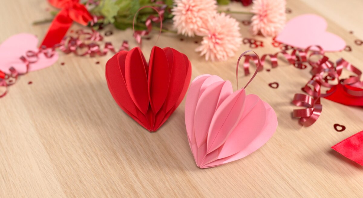 Rote und rosa Papierherzen stehen auf einem Holztisch, verziert mit pinken Schleifen, Blumen und Valentinstagsdekoration.
