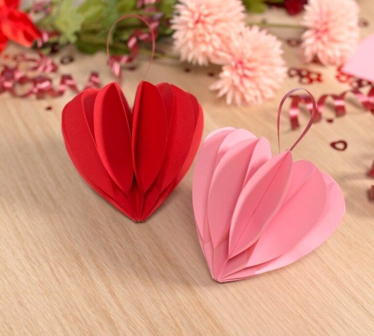 Rote und rosa Papierherzen stehen auf einem Holztisch, verziert mit pinken Schleifen, Blumen und Valentinstagsdekoration. | © bildderfrau.de