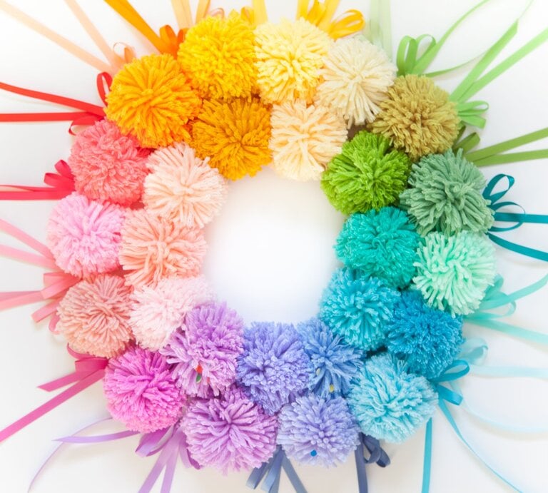 Regenbogenfarbener Pompon-Kranz aus weicher Wolle mit farbigen Geschenkbändern auf strahlend weißem Hintergrund arrangiert. | © Shutterstock/Kostikova Natalia