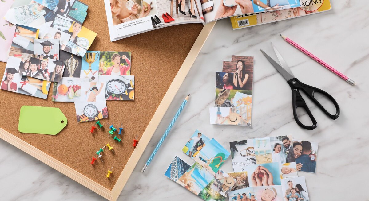 Auf einem Schreibtisch liegen ausgeschnittene Fotos, bunte Reißzwecken, Scheren und Zeitschriften für ein Vision Board.