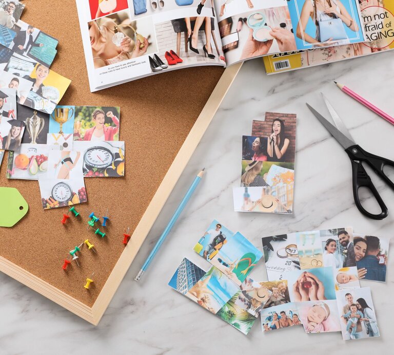 Auf einem Schreibtisch liegen ausgeschnittene Fotos, bunte Reißzwecken, Scheren und Zeitschriften für ein Vision Board. | © Shutterstock/ New Africa