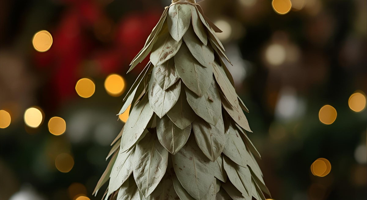 Kleiner Weihnachtsbaum aus getrockneten Lorbeerblättern mit goldener Sternspitze vor unscharfem Lichterhintergrund.