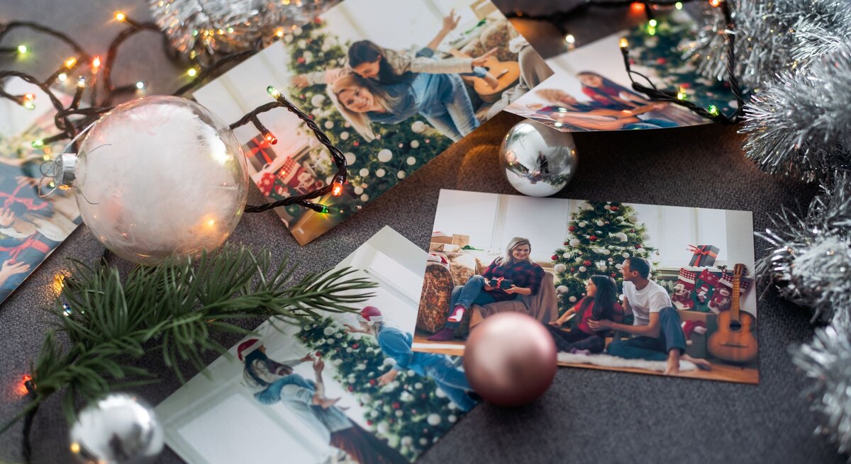 Weihnachtsfotos auf dunklem Stoff, umgeben von Kugeln, Lichterkette, Tannenzweig und silberner Girlande arrangiert.