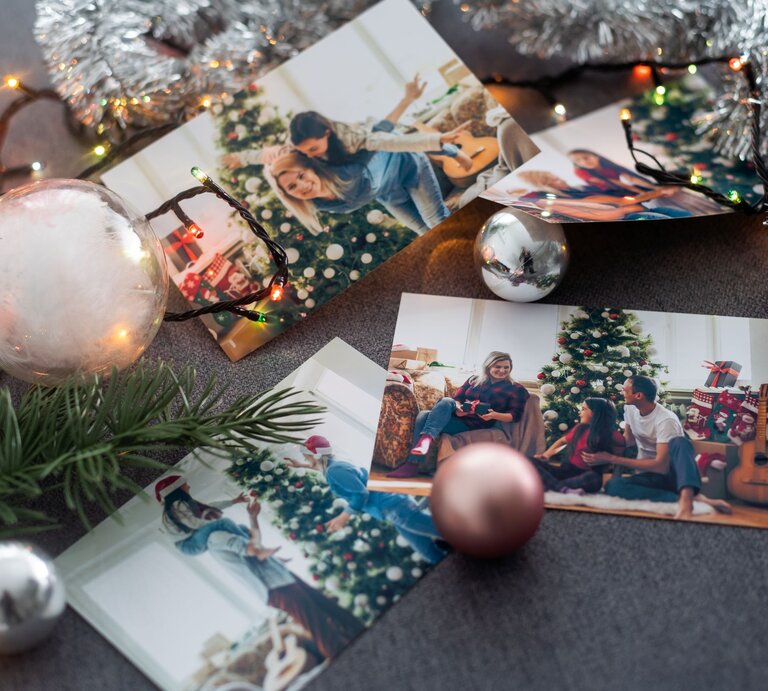 Weihnachtsfotos auf dunklem Stoff, umgeben von Kugeln, Lichterkette, Tannenzweig und silberner Girlande arrangiert. | © Shutterstock/Andrew Angelov