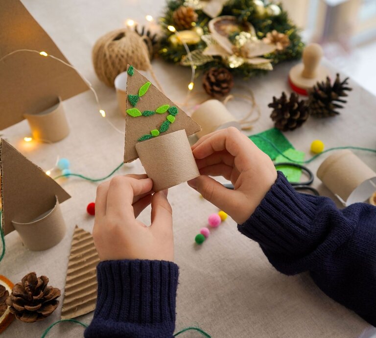 Weihnachtliche Teelichthalter mit Zapfen, Filz, Lichterkette und Trockenobst, Kind hält fertigen Baum aus Klopapierrollen in den Händen. | © Shutterstock/Irina Starikova1811
