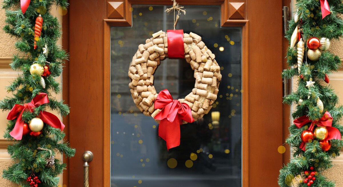 Weihnachtlich geschmückte Holztür mit Tannengirlanden und einem Kranz aus Korken, verziert mit roter Schleife.