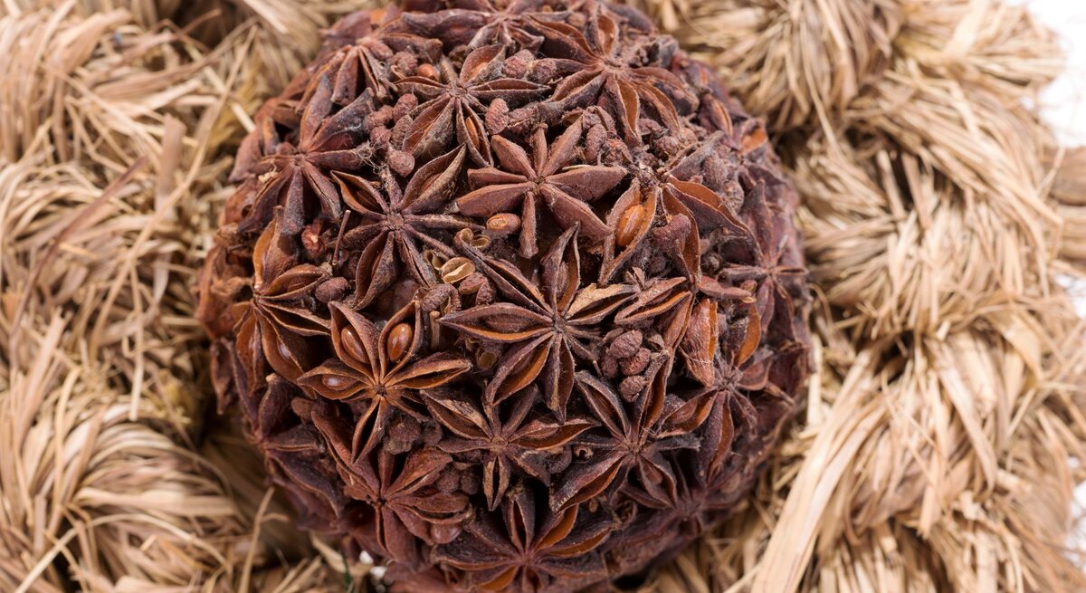 Runde Kugel aus getrocknetem Sternanis und Gewürznelken liegt dekorativ auf einem Nest aus hellem Strohgeflecht