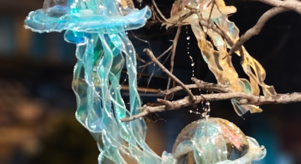 Drei schimmernde Quallenlaternen aus transparentem Stoff hängen leuchtend zwischen kahlen Ästen im Dunkel der Nacht.