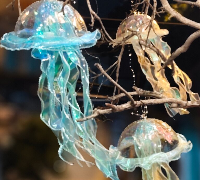 Drei schimmernde Quallenlaternen aus transparentem Stoff hängen leuchtend zwischen kahlen Ästen im Dunkel der Nacht. | © Shutterstock/ Sobin2002