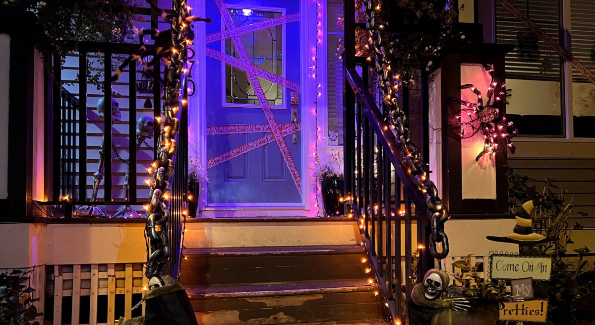 Hauseingang gestalten für Halloween: Mit Lichterketten, Ketten, Skeletten und Spinnennetzen gruselig geschmückter Hauseingang bei Nacht.