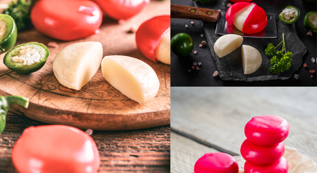 Runde Mini-Käselaibe mit rotem Wachs, teils aufgeschnitten, liegen gestapelt oder auf Brettern mit Kräutern, Chili und Salz.