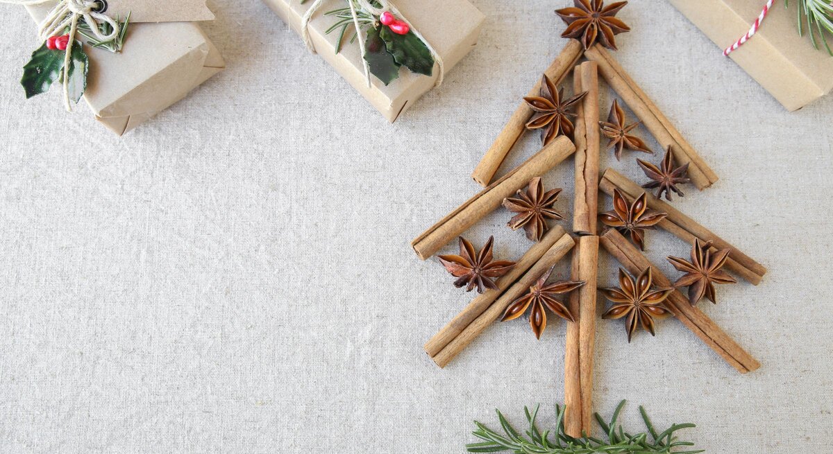 Aus Zimtstangen, Sternanis und Rosmarin gelegener Weihnachtsbaum auf Leinentuch, daneben schlicht verpackte Geschenke.