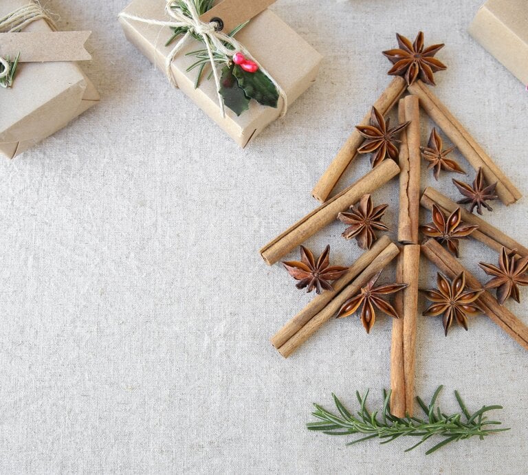 Aus Zimtstangen, Sternanis und Rosmarin gelegener Weihnachtsbaum auf Leinentuch, daneben schlicht verpackte Geschenke. | © Shutterstock/SewCreamStudio