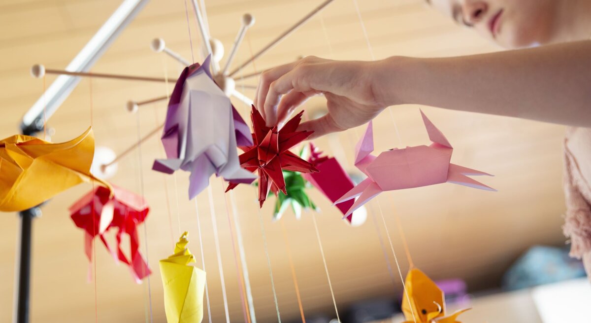 Teenager-Mädchen bastelt ein Mobile fürs Babybett mit selbstgemachten bunten Origami-Skulpturen