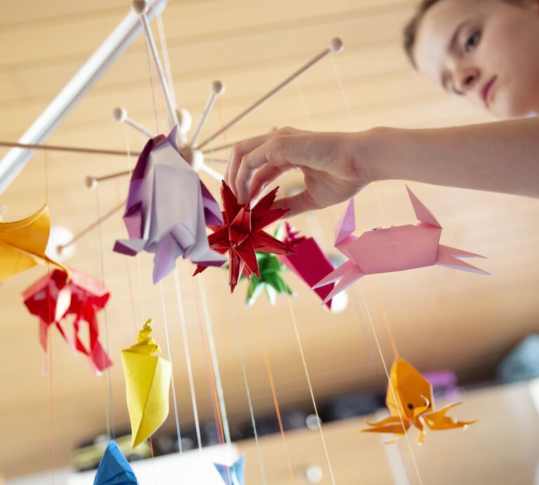 Teenager-Mädchen bastelt ein Mobile fürs Babybett mit selbstgemachten bunten Origami-Skulpturen | © Getty Images/Elva Etienne