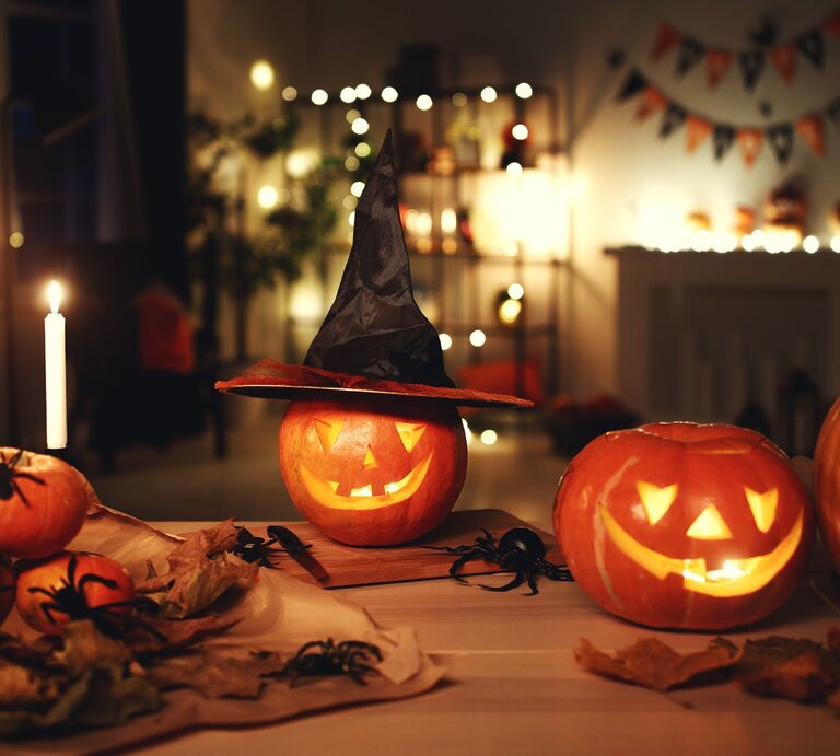 Solarleuchten basteln: Drei leuchtende Kürbislaternen mit geschnitzten Gesichtern, einer mit Hexenhut, auf herbstlich dekoriertem Tisch bei Kerzenlicht. | © Shutterstock/Evgeny Atamanenko