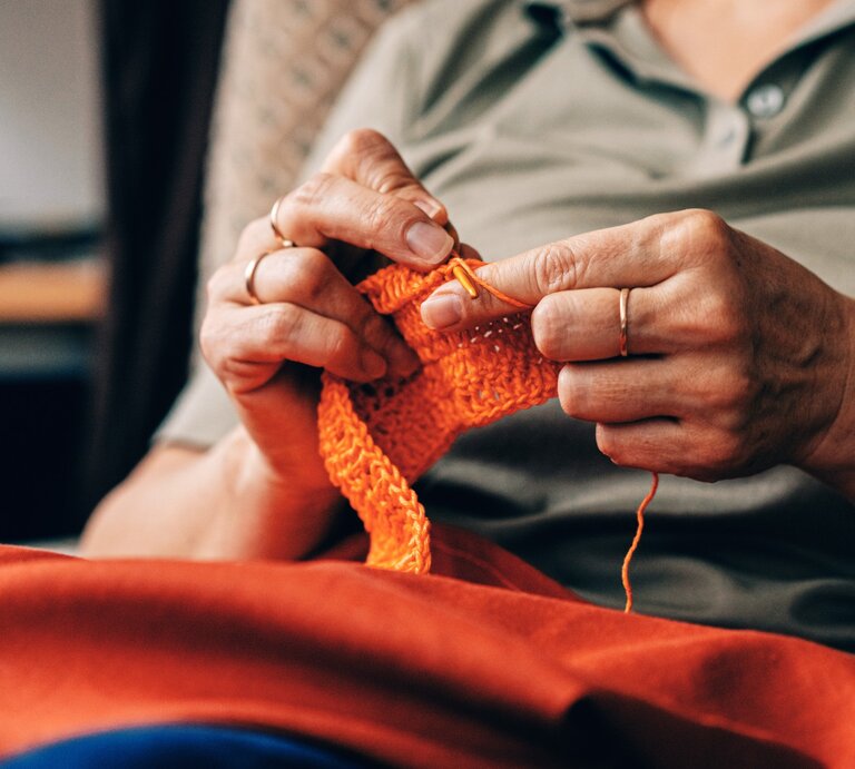 Zu sehen ist eine Frau mittleren Alters, die gerade strickt. | © GettyImages/Olena Malik
