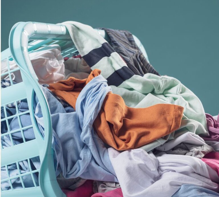 Nahaufnahme eines Korbs mit frisch gefalteten, weichen Handtüchern in Grau und Rosa, gehalten von einer Person in lässiger Kleidung vor neutralem Hintergrund. | © Collage: bildderfrau.de; Canva