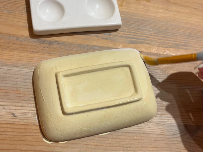 Eine gelbe Keramikschale wird mit einem Pinsel bemalt, daneben liegt eine weiße Farbpalette auf einem Holztisch | © Kaja Wundersitz/ Linda Pötzsch/ BIld der Frau