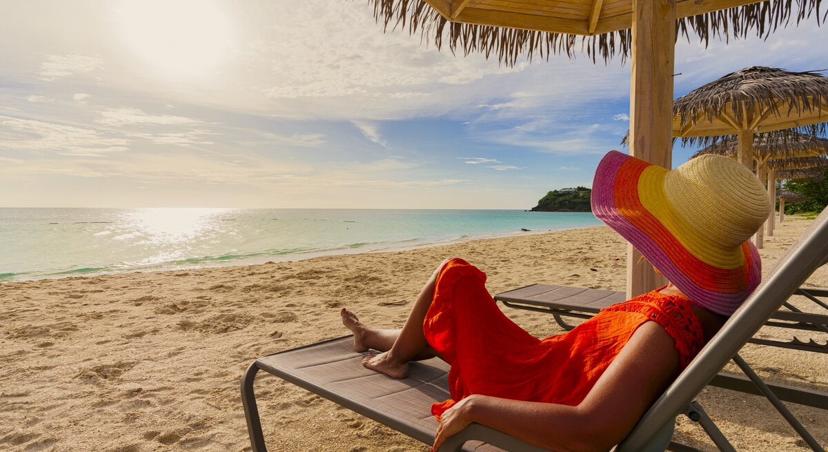 Zu sehen ist eine Frau mit Sonnenhut, die am Strand liegt