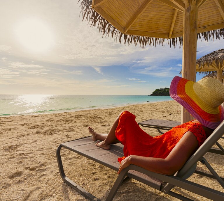 Zu sehen ist eine Frau mit Sonnenhut, die am Strand liegt | © GettyImages/Roberto Moiola / Sysaworld
