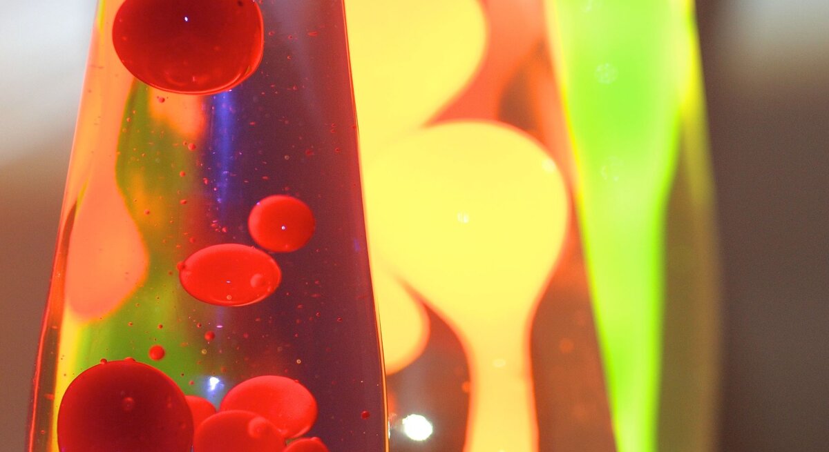 Drei Lavalampen mit leuchtend roter, gelber und grüner Wachsmischung blubbern bunt in flüssigem Licht vor dunklem Hintergrund.