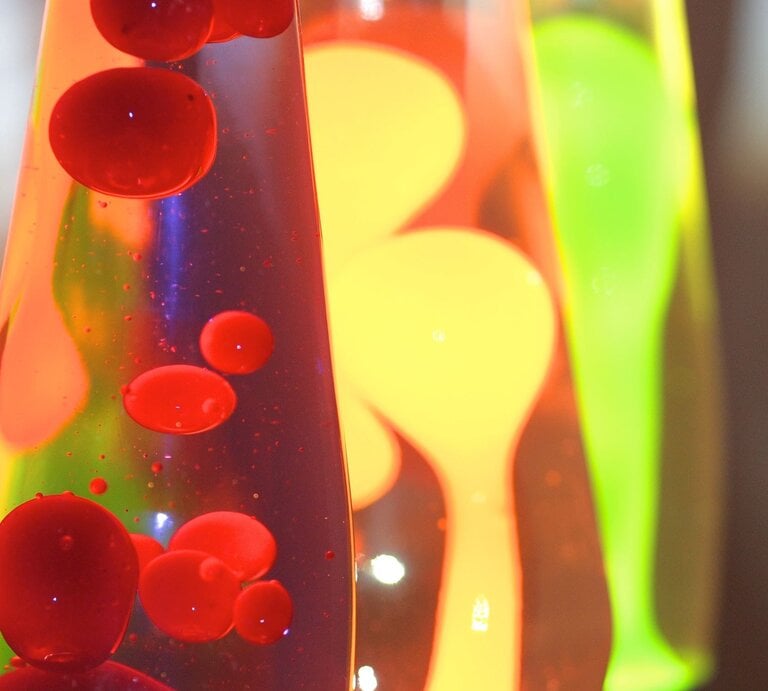 Drei Lavalampen mit leuchtend roter, gelber und grüner Wachsmischung blubbern bunt in flüssigem Licht vor dunklem Hintergrund. | © Adobe Stock/ focus finder