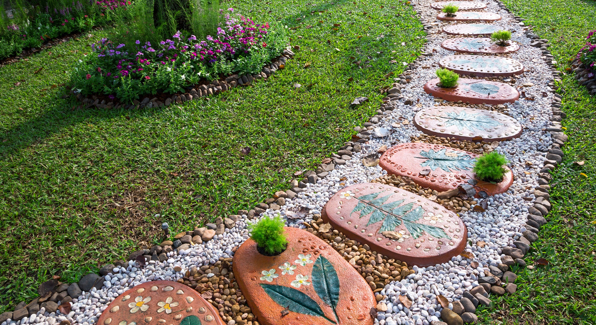Geschwungener Gartenweg aus bunten Trittsteinen mit Blumenmotiven, umrahmt von Kieseln und gepflegtem Rasen.