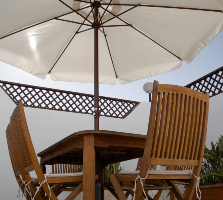 Weiße Sonnenschirme auf Balkon und Terrasse spenden Schatten über Holzmöbeln, in Nahaufnahme und Totale aus sommerlicher Perspektive. | © Canva/Collage:bildderfrau.de