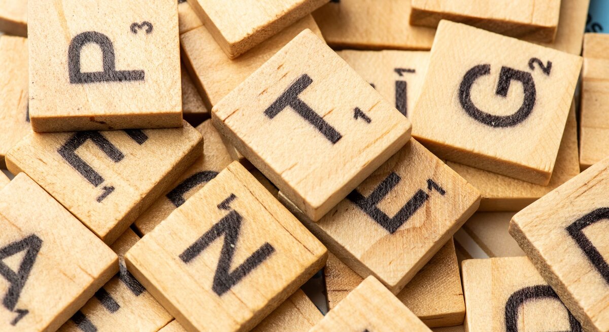 Ein Haufen hölzerner Scrabble-Buchstabensteine mit schwarzen Lettern liegt chaotisch durcheinander.