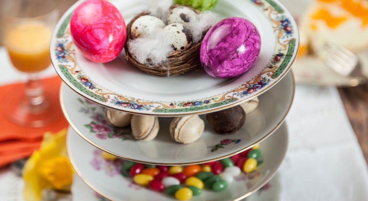 Eine elegante Etagere aus verzierten Porzellantellern mit Ostereiern, Pralinen, Macarons und bunten Süßigkeiten.