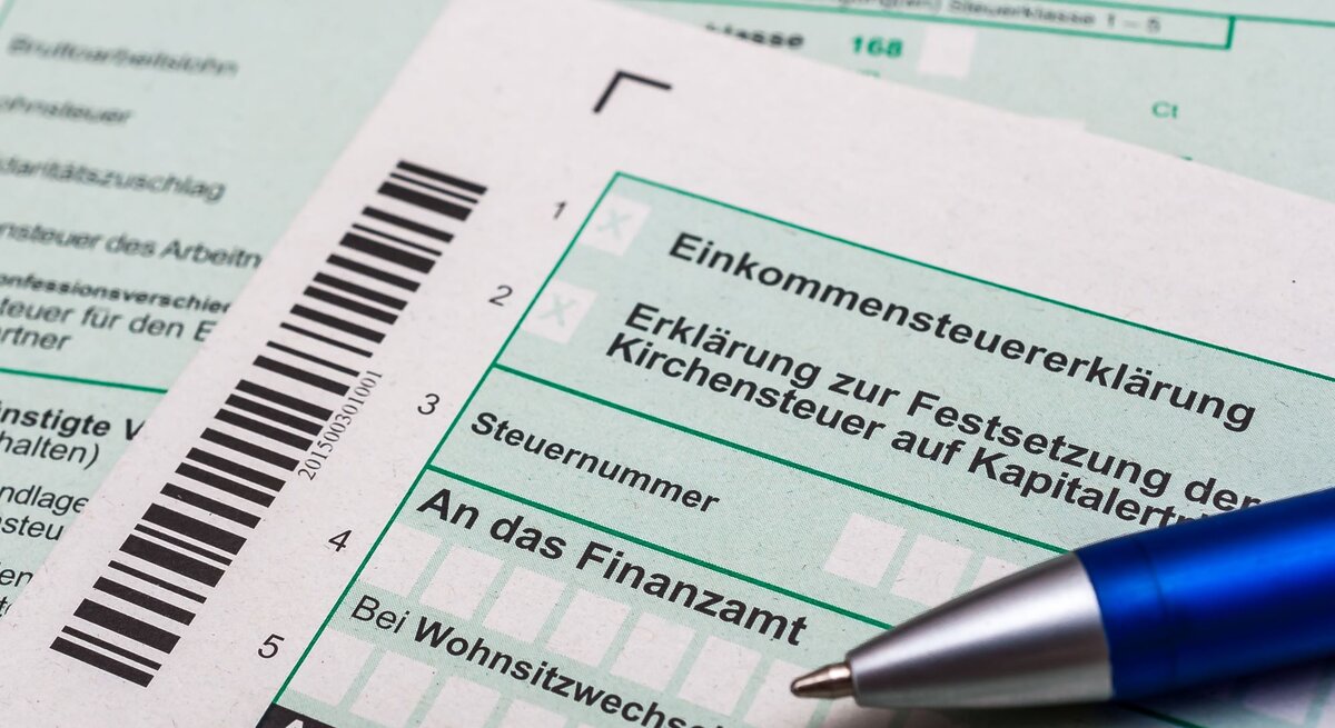 Nahaufnahme von deutschen Steuerformularen zur Einkommensteuererklärung mit einem blauen Kugelschreiber darauf.