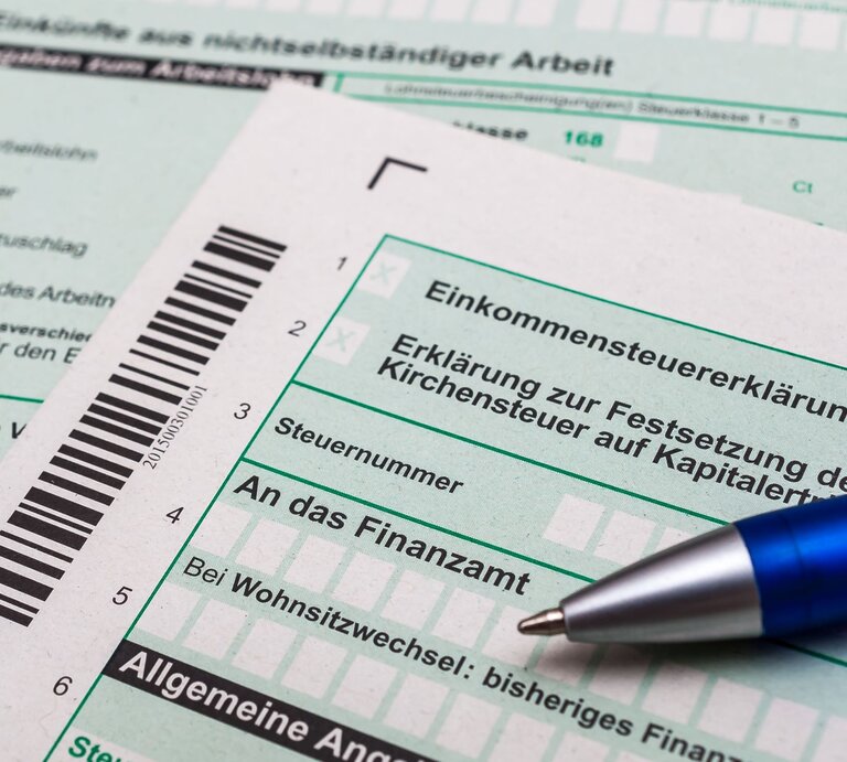 Nahaufnahme von deutschen Steuerformularen zur Einkommensteuererklärung mit einem blauen Kugelschreiber darauf. | © Adobe Stock/Stockfotos-MG