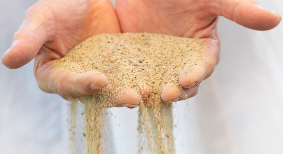 Zwei offene Hände lassen feinen, goldbraunen Sand langsam zwischen den Fingern hindurchrieseln.