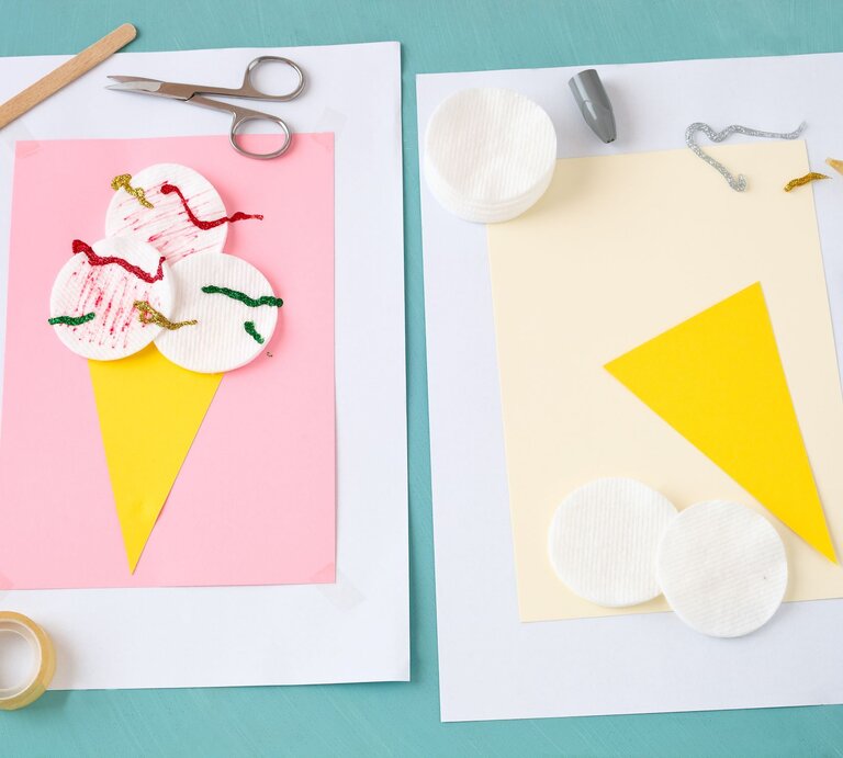 Bastelprojekt auf türkisfarbenem Untergrund: Zwei Papierblätter mit Eiswaffel-Collagen aus gelbem Karton und Wattepads, verziert mit Glitzerkleber. | © Adobe Stock/rainbow33